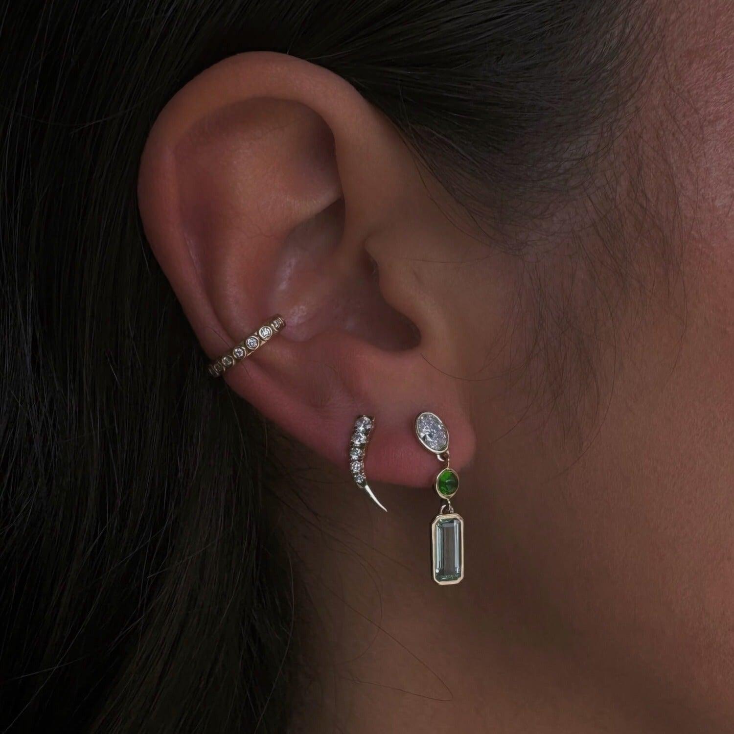 Image of a Marrow Fine ear stack on ear. White diamond ear cuff, white diamond ear crawler, and Oval diamond and Beryl Bezel Set Dangle Earrings.