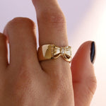 Image of pointer finger with the Bow Cigar Band on in 14k yellow gold. The bow pops out of the band and has small set white diamonds in the center. 