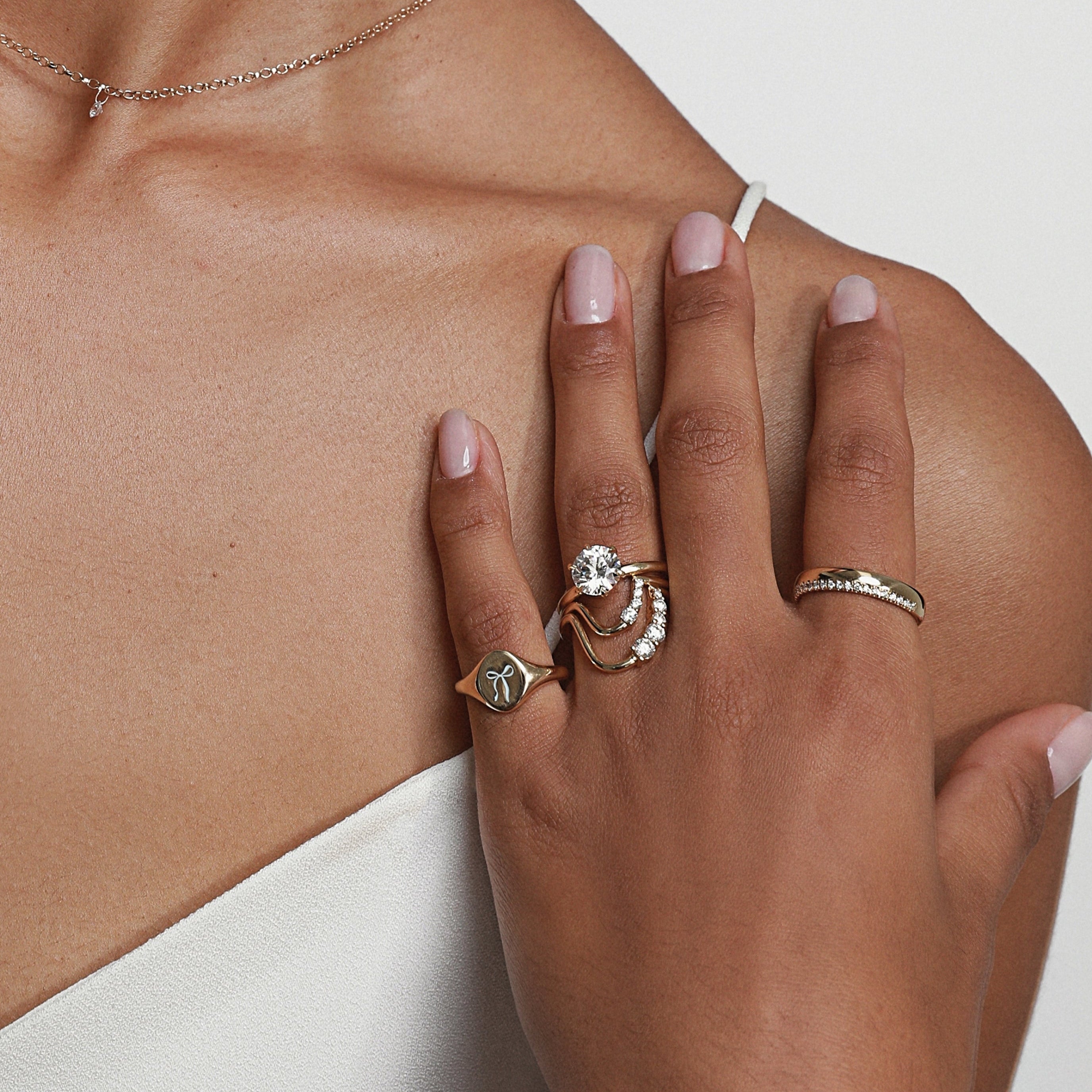 Close up of woman's hand resting against her collarbone, with multipole Marrow Fine Rings styled, the Trunk Show Exclusive Signet on her pinky