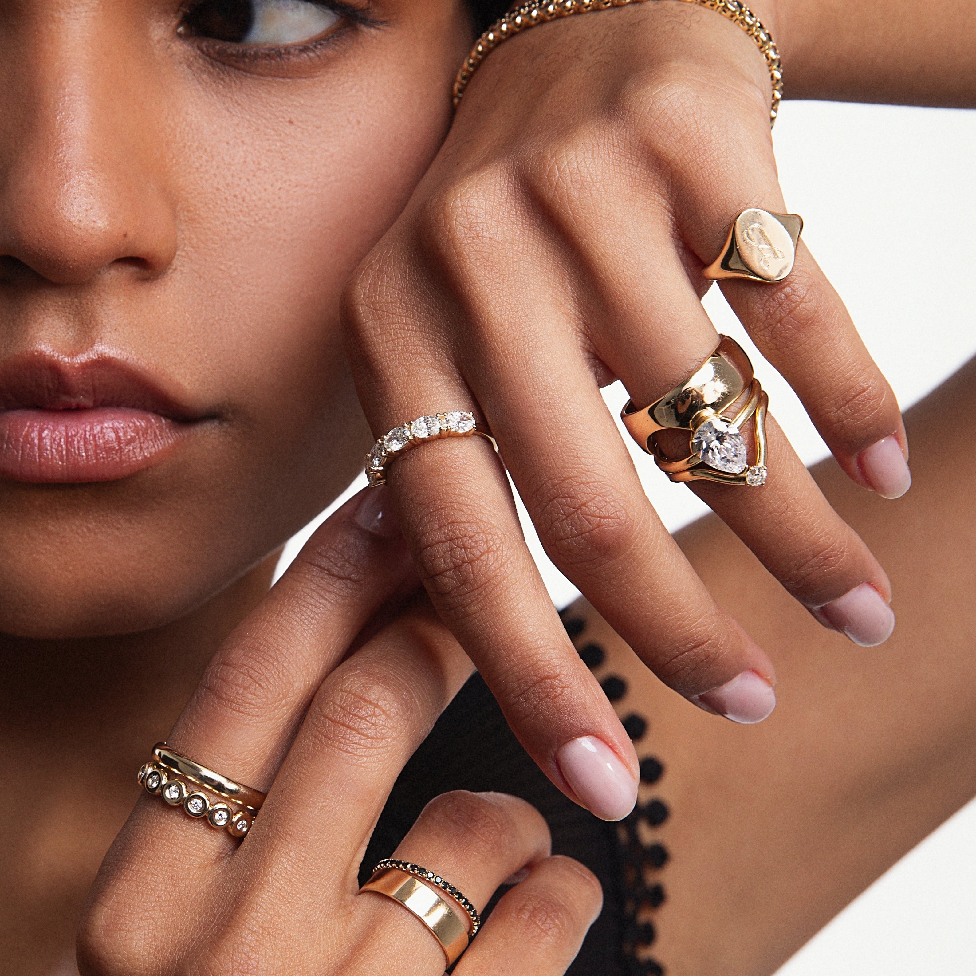 Close up of woman resting hands against her face featuring styled Marrow Fine rings and bracelets