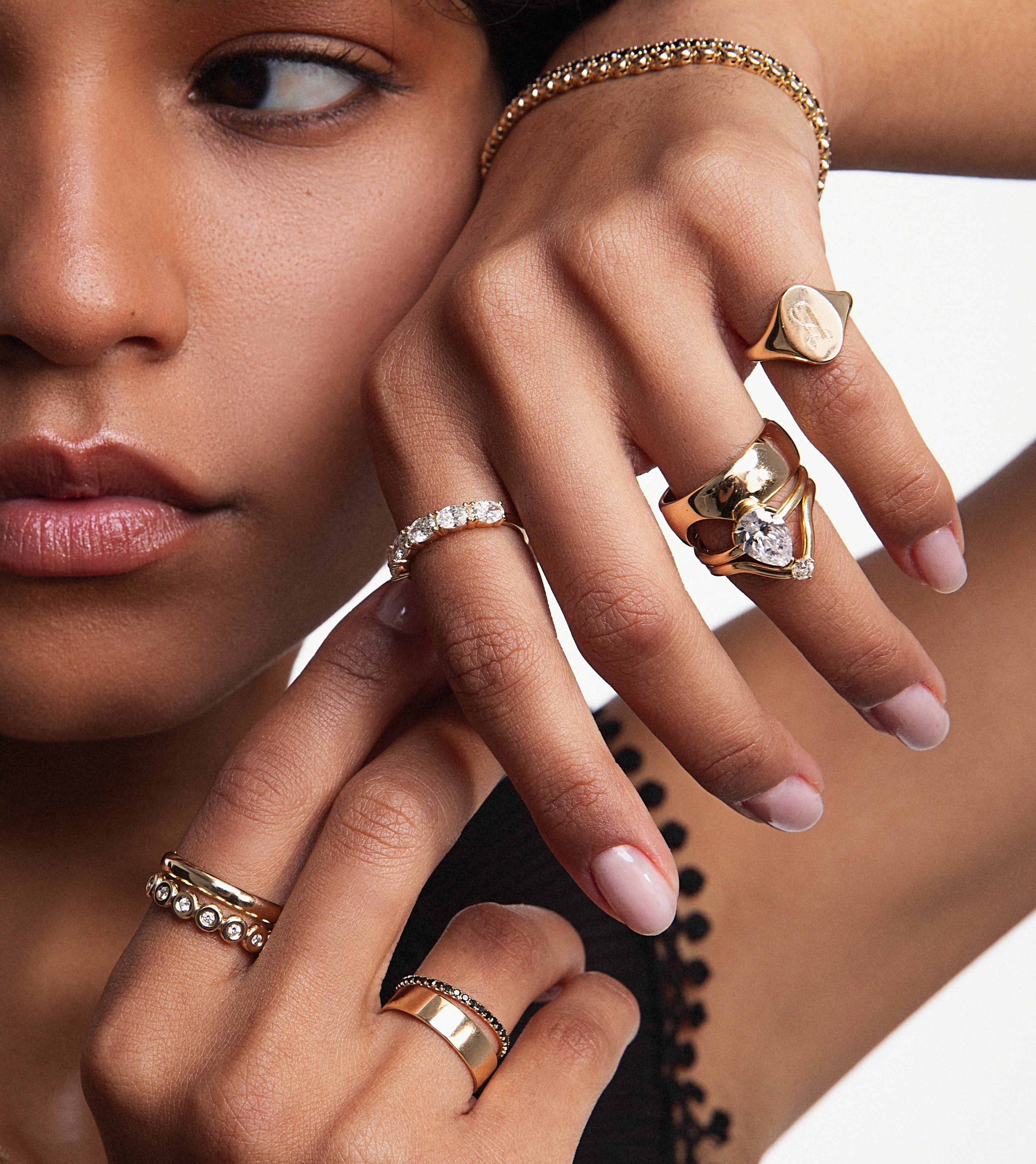 Close up of woman resting hands against her face featuring styled Marrow Fine rings and bracelets